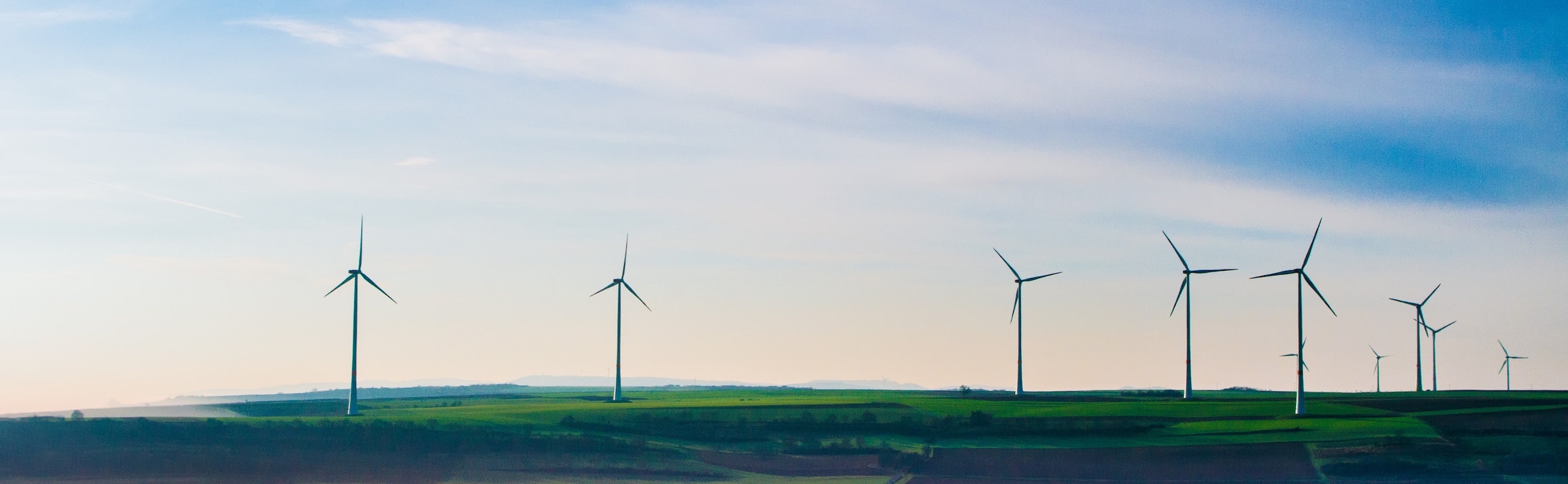 Wind turbines on green grass field under white clouds and blue sky