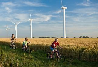 Children riding bikes through field with backdrop of wind turbines