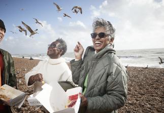 People eating fish and chips on the beach surrounded by seagulls