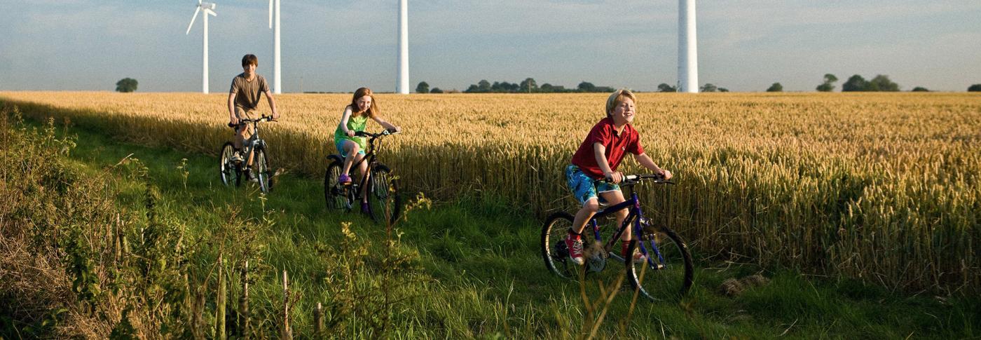 Children riding bikes through field with backdrop of wind turbines