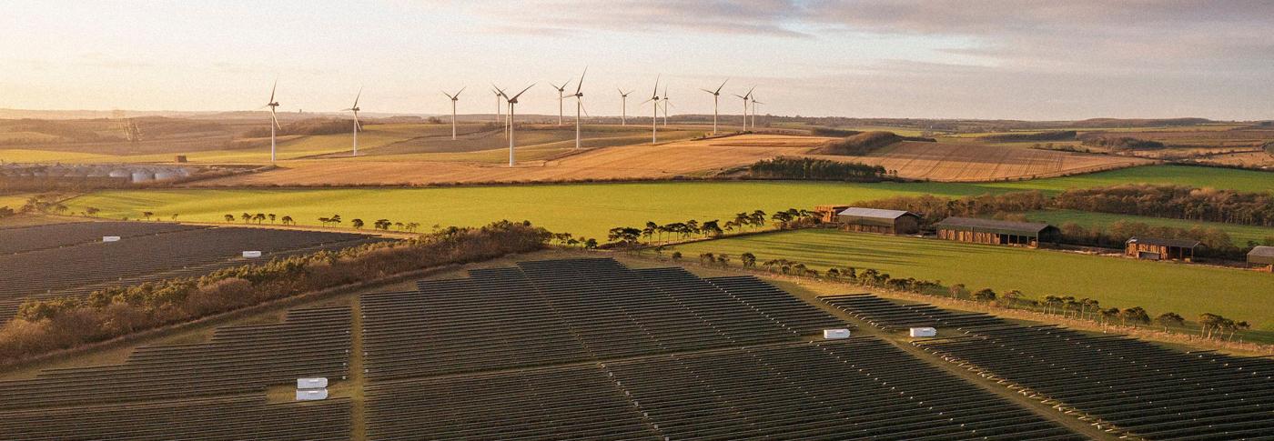 Solar panels and wind turbines in fields with the sunset in sky