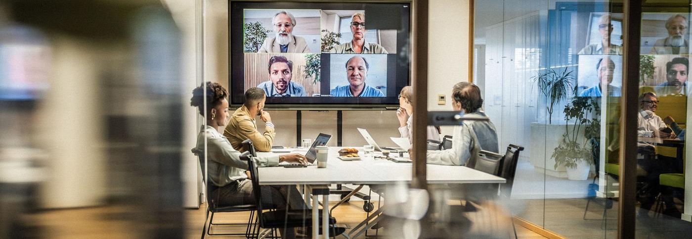 Team sat in a meeting room with a few people on the big tv