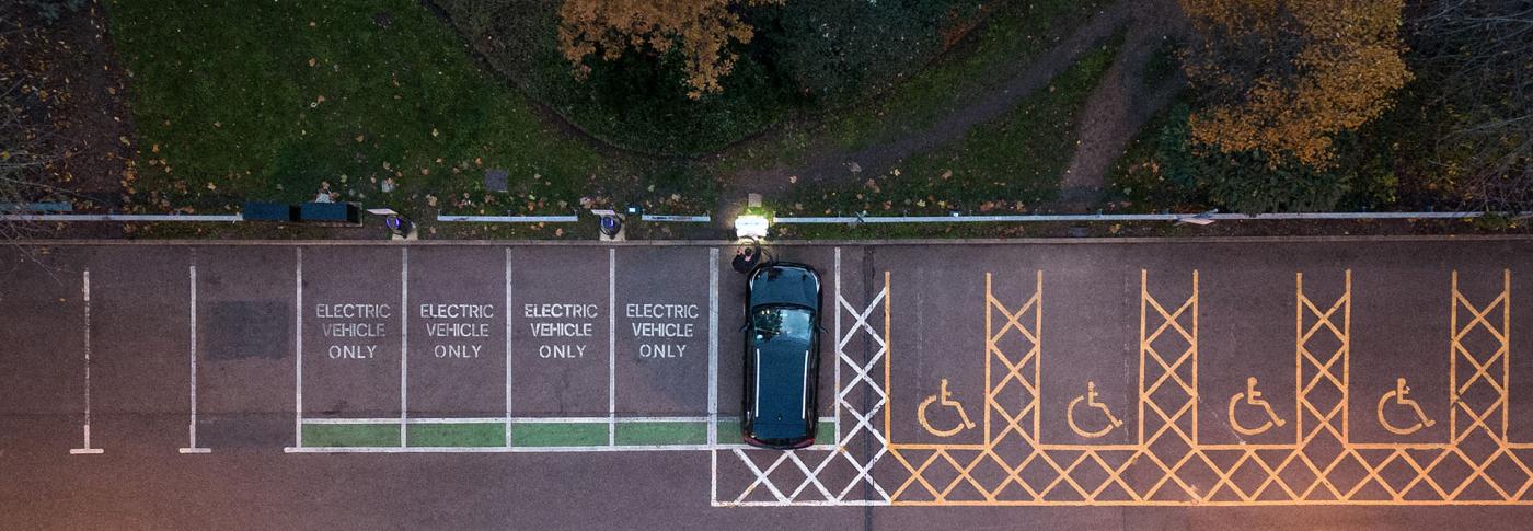 Ariel image of car park and person putting their EV car on charge