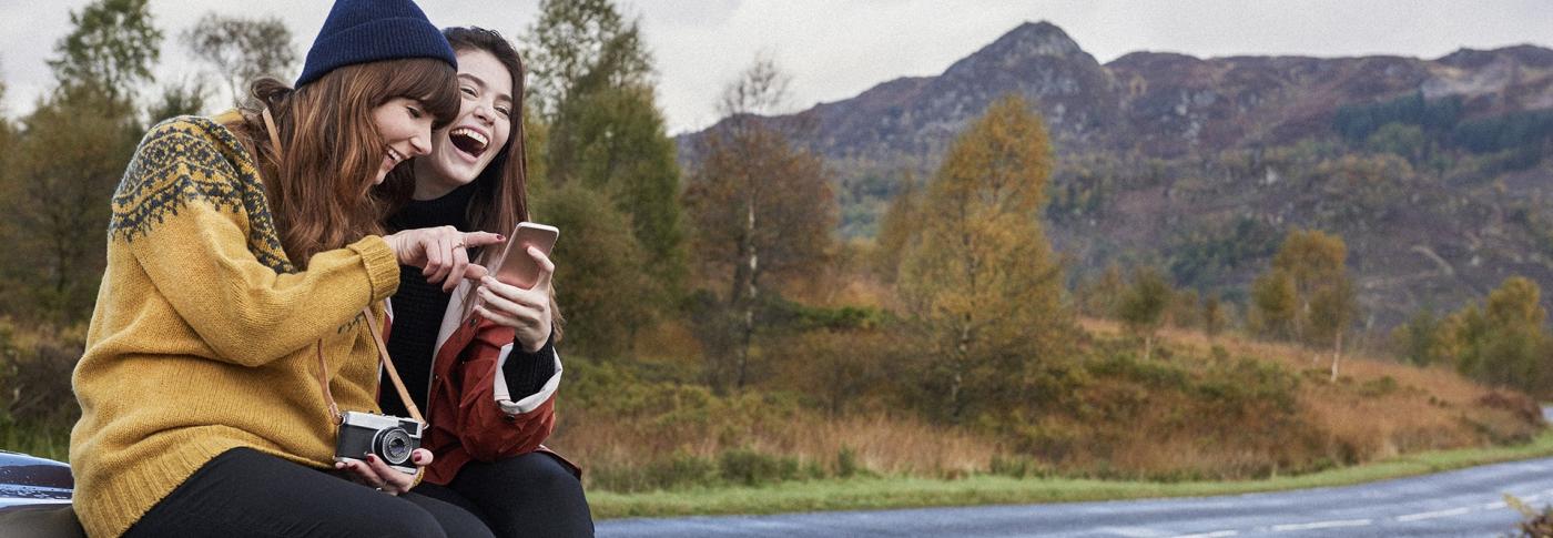 Ladies sat on car bonnet looking and taking photos of the mountains