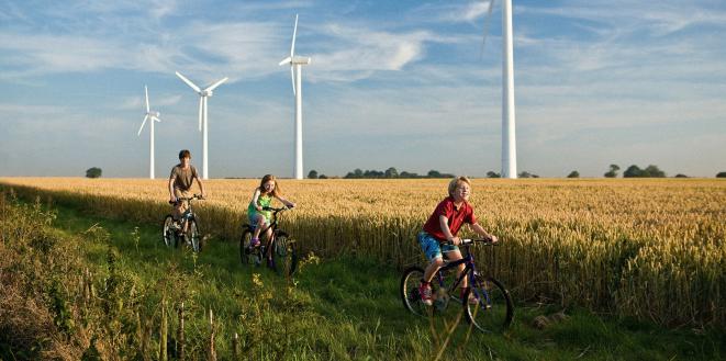 Children riding bikes through field with backdrop of wind turbines