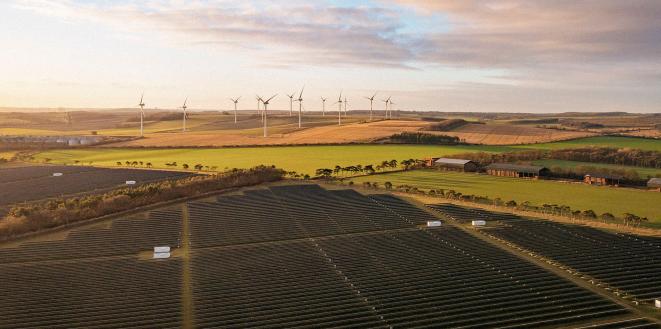 Solar panels and wind turbines in fields with the sunset in sky