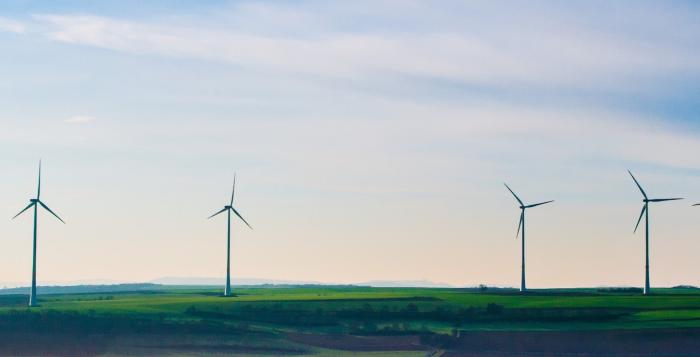 Wind turbines on green grass field under white clouds and blue sky