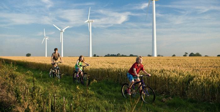 Children riding bikes through field with backdrop of wind turbines