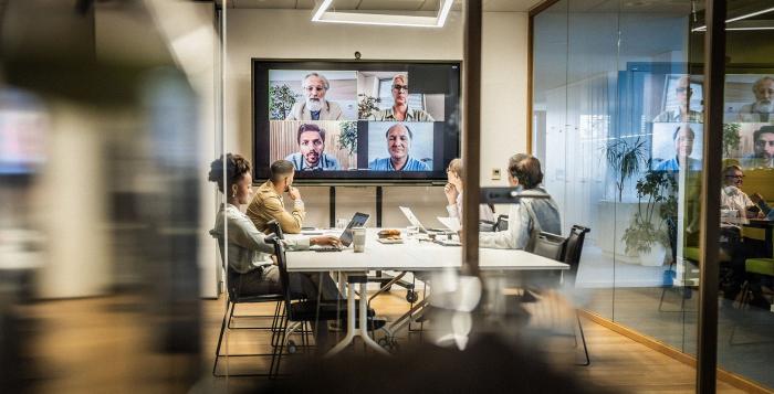 Team sat in a meeting room with a few people on the big tv