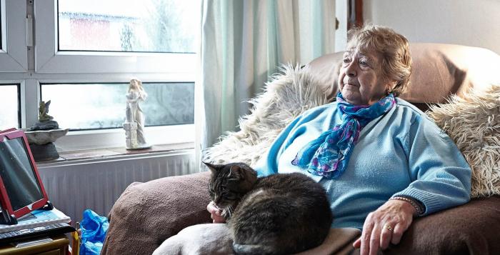 Older lady sat in armchair with cushion on her lap on cushion is a cat