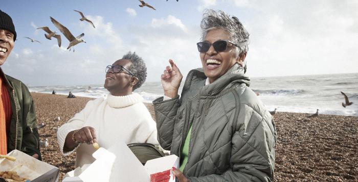 People eating fish and chips on the beach surrounded by seagulls