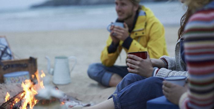 People sat around a fire on the beach drinking hot drinks