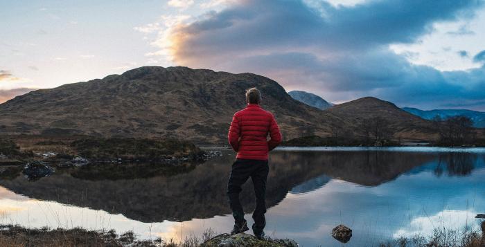 Person stood on top of mountain with lake below showing reflections of sky